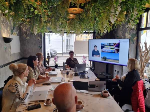 Joanne Wharam sat at the head of a table next to a monitor delivering team building training to 5 people