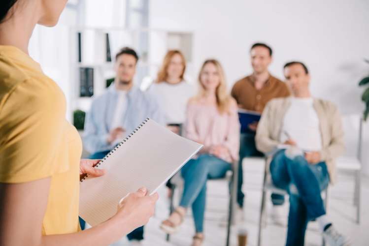 Lady holding a piece of paper in front of a team sat down